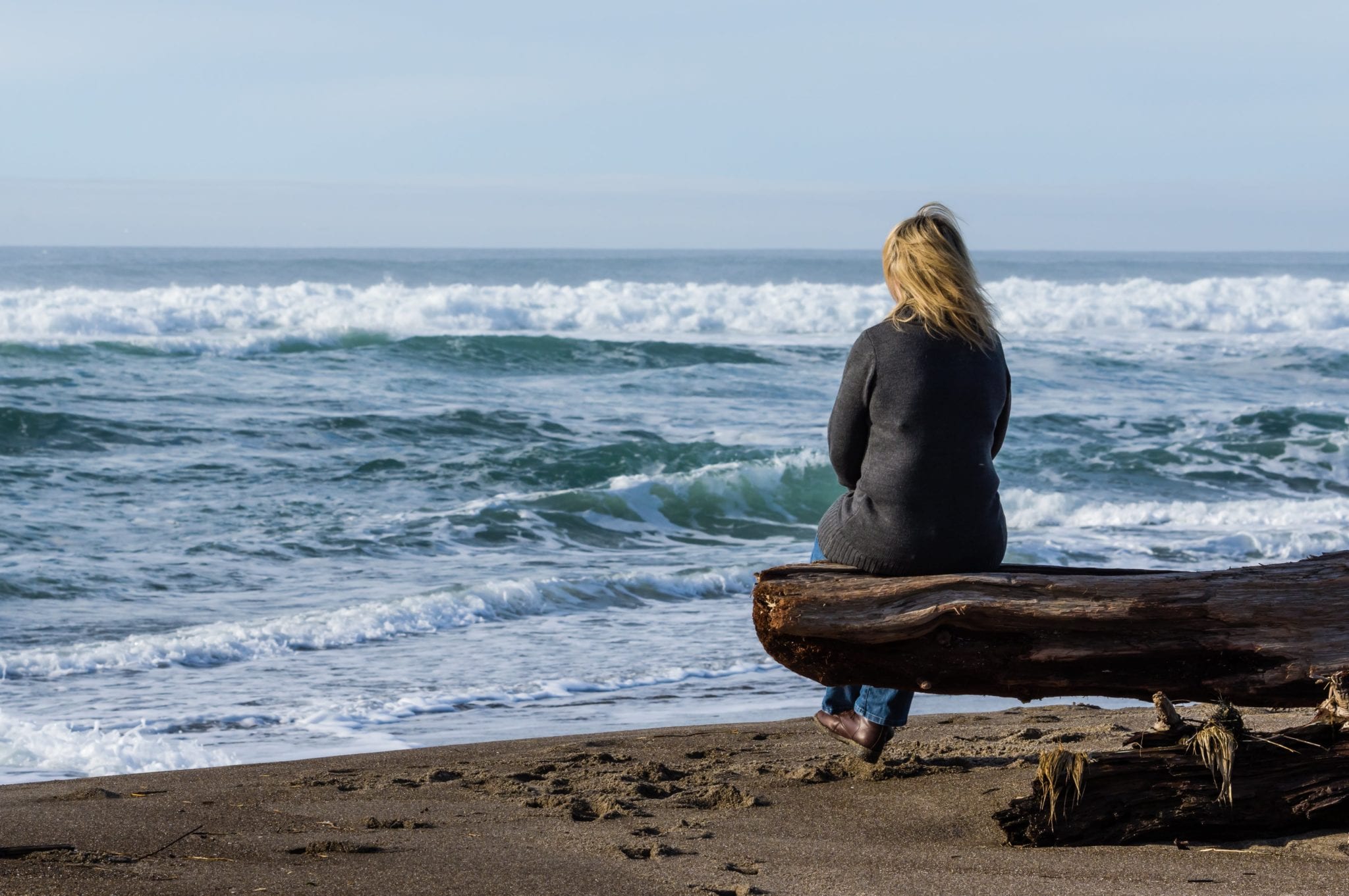 Woman sitting on a driftwood log | Clarity Hearing
